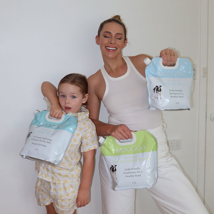 Smiling woman and child holding MooGoo Natural Milk Wash and Conditioner refill packs, eco-friendly bulk skincare option
