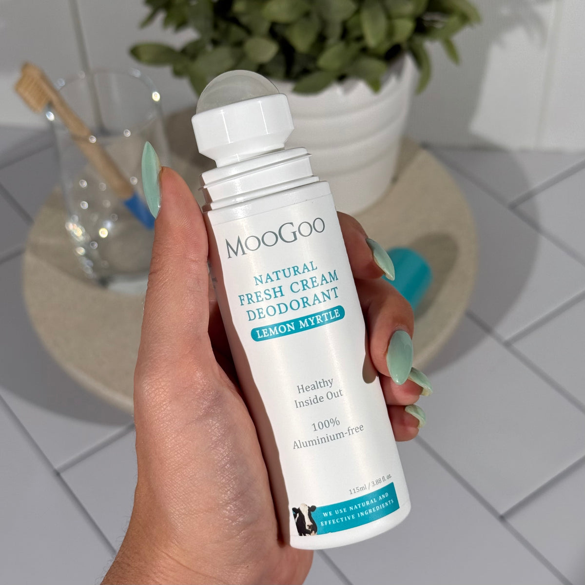 MooGoo Lemon Myrtle Fresh Cream Deodorant 115ml held by a hand with a tiled background