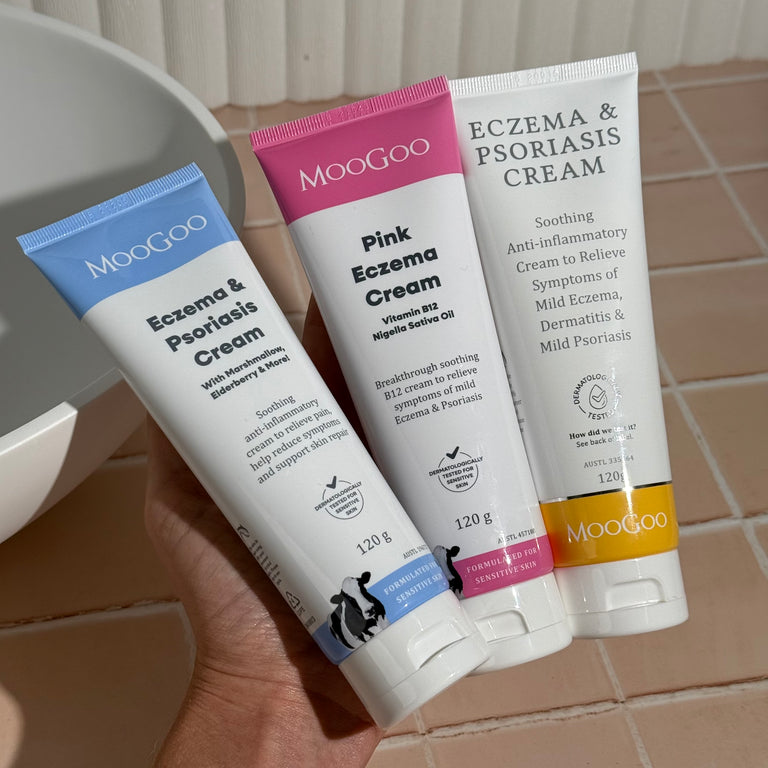 MooGoo Eczema and Psoriasis Cream Marshmallow Elderberry, Eczema and Psoriasis Cream Gotu Kola Chamomile, and Pink Eczema Cream Vitamin B12 held in one hand, soothing cream for sensitive eczema and psoriasis prone skin