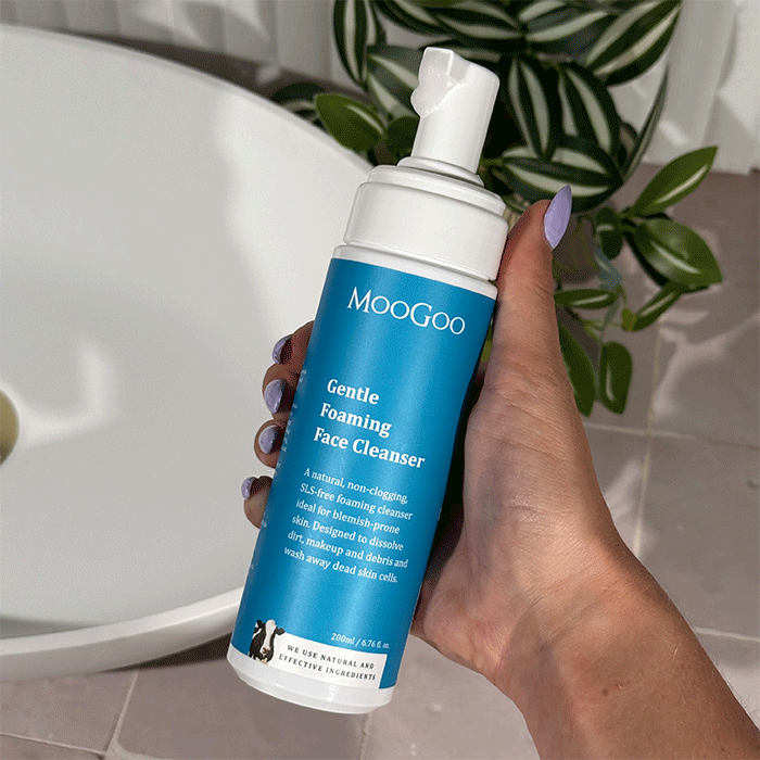 MooGoo Gentle Foaming Face Cleanser held in hand near bath, natural SLS-free cleanser for fresh, blemish-free skin