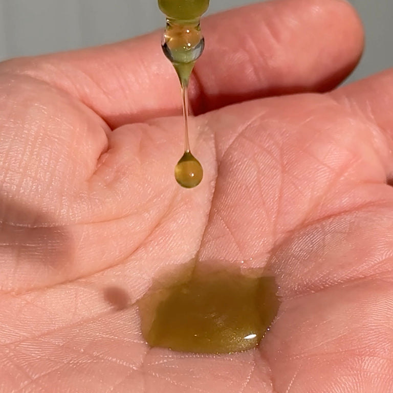 MooGoo 100% Tamanu face oil droplet falling onto hand.