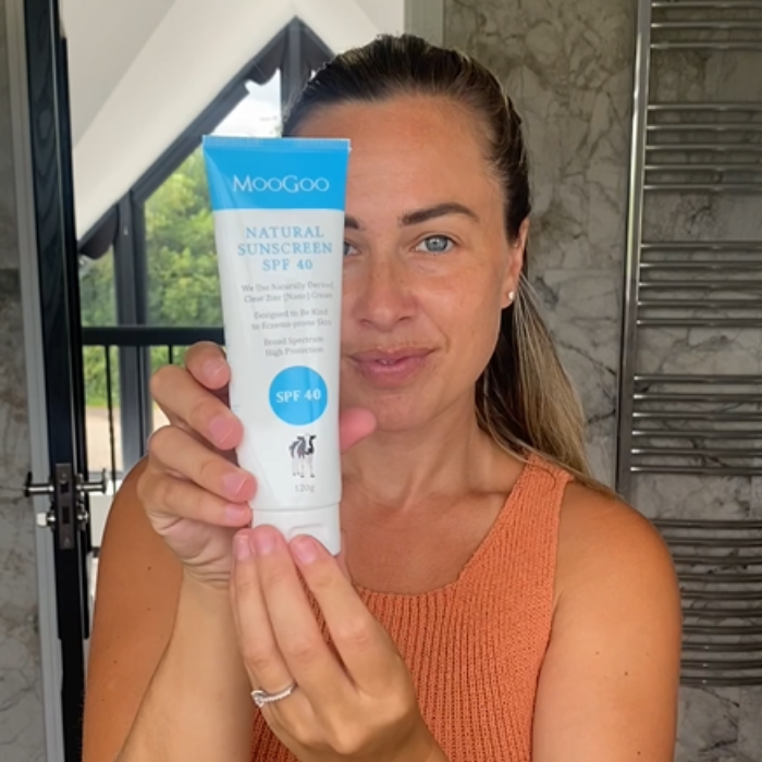 Smiling woman holding MooGoo Clear Zinc Sunscreen SPF 40, natural zinc oxide sunscreen for sensitive skin with broad spectrum UVA UVB protection