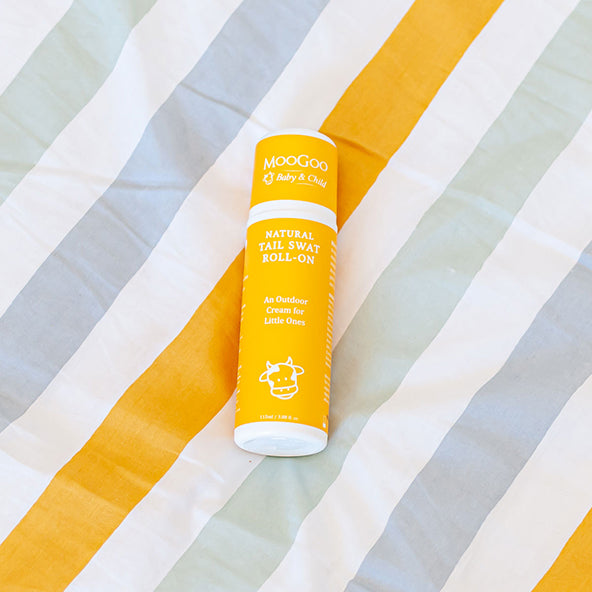 MooGoo Tail Swat Roll-On placed on yellow and white striped blanket, gentle insect repellent cream for children and families, natural outdoor skincare