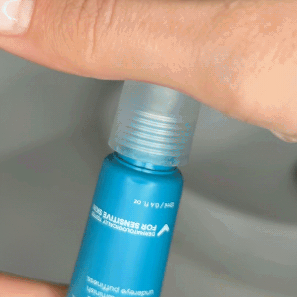 Close-up of a woman's face with a blue skincare rollerball tube being used to apply MooGoo 3-in-1 Peptide Eye Serum under her eye. Made with Vitamin C, Copper Tri-Peptide, Argireline Amplified and Vitamin K to brighten dark circles, reduce fine lines and wrinkles, and diminish under eye puffiness.