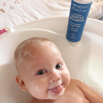 Smiling baby in bath with shampoo foam on scalp and MooGoo Gentle Shampoo bottle behind, natural tear-free formula for delicate newborn and child skin
