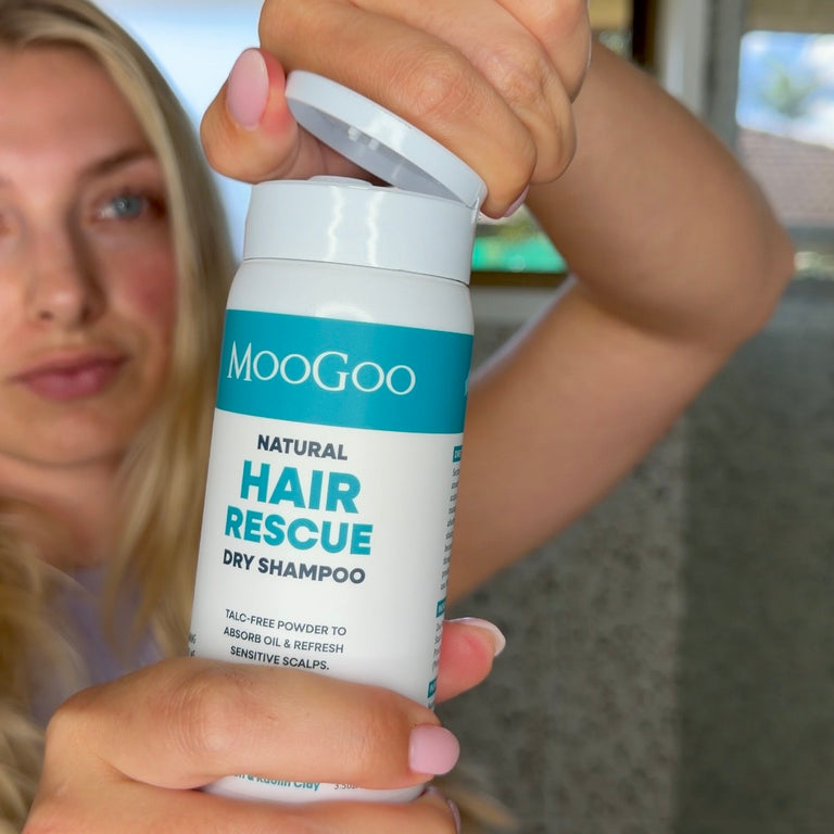 Woman Holding a turquoise and white bottle of MooGoo Hair Rescue Dry Shampoo with the lid open. Natural talc free formula. Adds volume and texture without aerosols. 