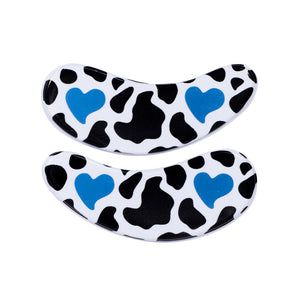 Two curved reusable eye mask patches with a black and white cow print pattern and two blue heart designs, shown on a plain white background. To lock in moisture and hydration from skincare and eye serums. 