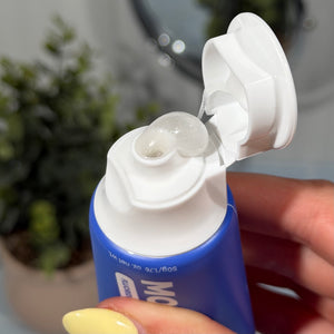 Hand holding a tube of MooGoo Blueberry Smoothie kids toothpaste and squeezing out the product. Healthy habit building, tastes like blueberries. Fluoride-free formula, safe for kids.