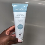 MooGoo Skin Milk Udder Cream tube in hand over plain bathroom background, gentle hydrating cream for restoring skin softness and health.