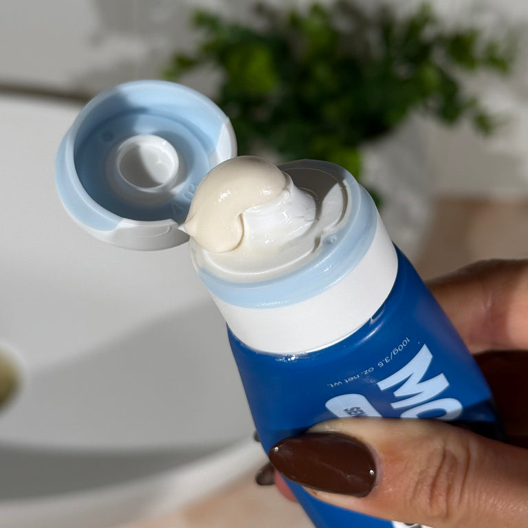 MooGoo Fluoride-Free Sensitive Peppermint Whitening toothpaste tube with toothpaste being squeezed out, held by a hand.