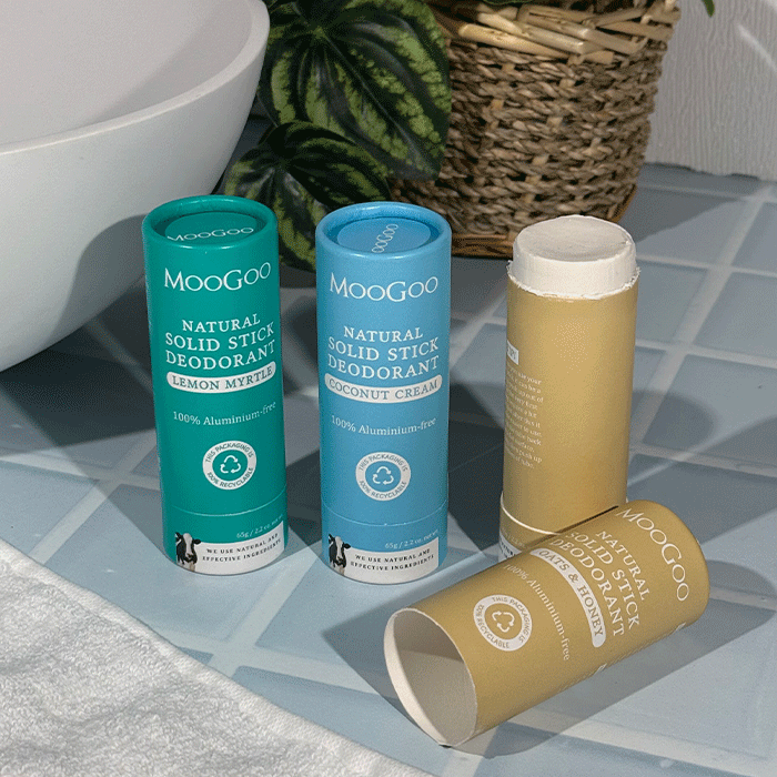 MooGoo 65g Natural Solid Stick Deodorants displayed on a bathroom counter with a plant partially in the background. 100% aluminium free, plastic-free natural odour control.