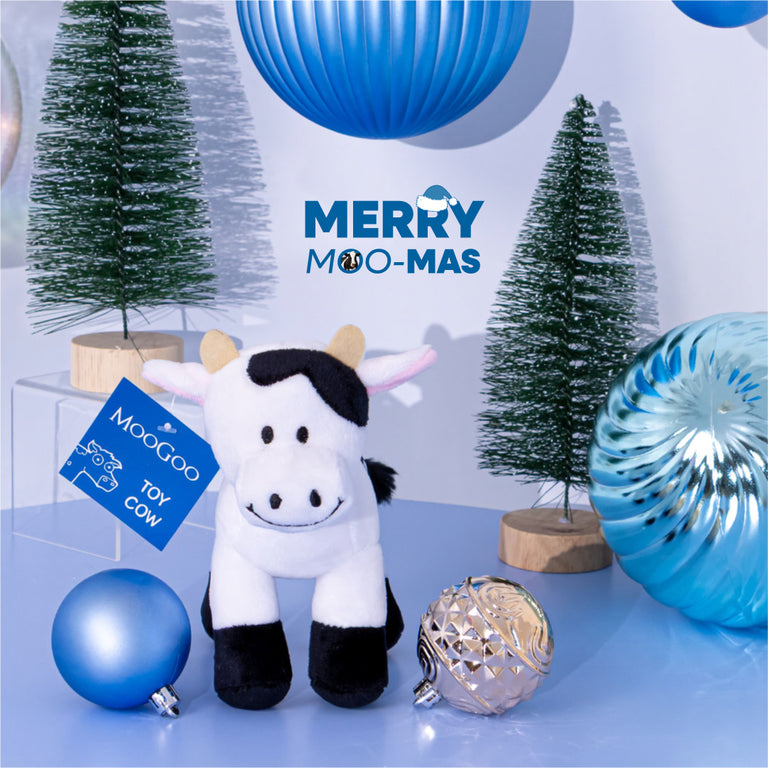 MooGoo Toy Cow photographed on Christmas-themed background, small plush cow toy for children, 15cm tall, soft, cuddly and safe, ideal as a baby or toddler gift.