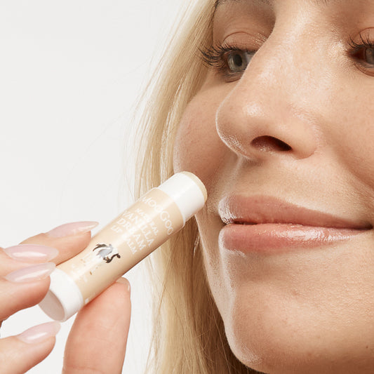 Woman applying MooGoo Vanilla Dream Lip Balm bon clean backdrop, natural moisturising lip balm for dry chapped lips made with edible safe ingredients, petroleum free, all natural.