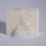 MooGoo Soothing Cleansing Bar Goat’s Milk covered in foam on neutral surface, natural soap substitute to hydrate and calm sensitive skin.